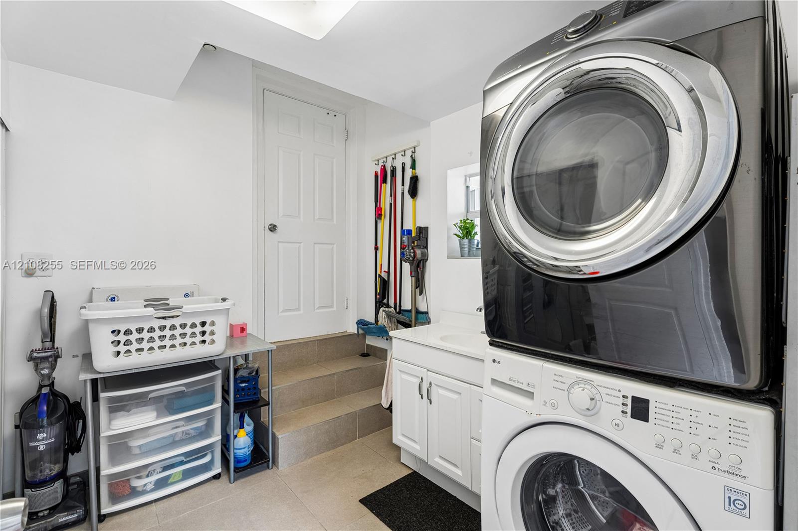 Laundry area featuring a stacked washer and dryer, white shaker-style cabinetry, an integrated basin sink, and tiled flooring