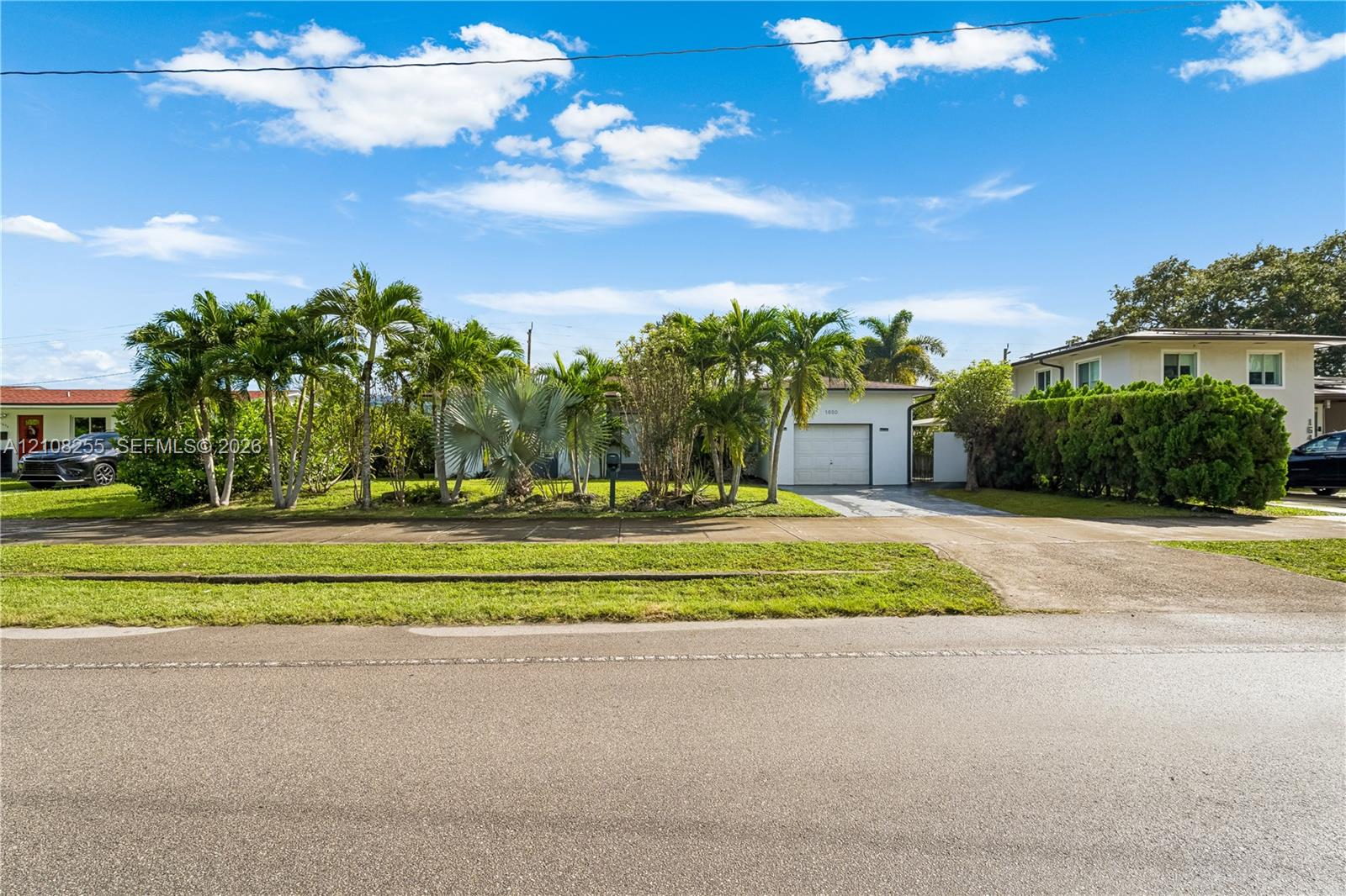 Exterior of a single-story residence featuring a concrete driveway, attached garage, manicured lawn, and mature palm landscaping