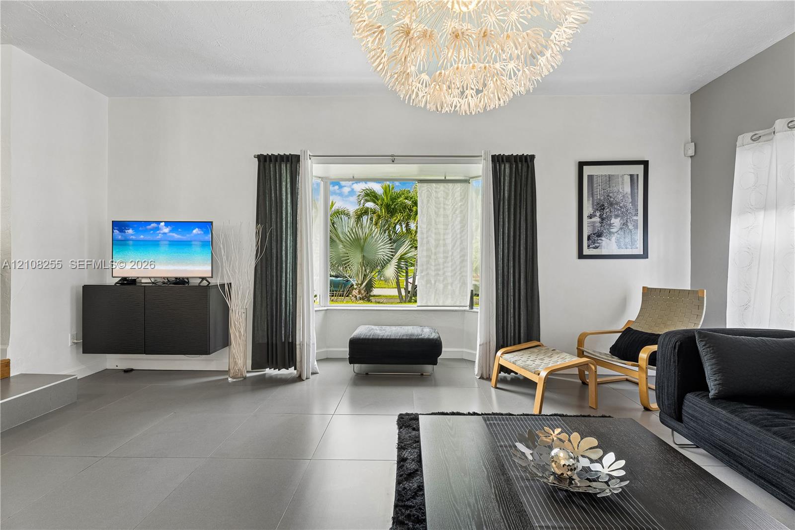 Living space featuring large format tile flooring, a prominent bay window, and a modern tiered chandelier fixture