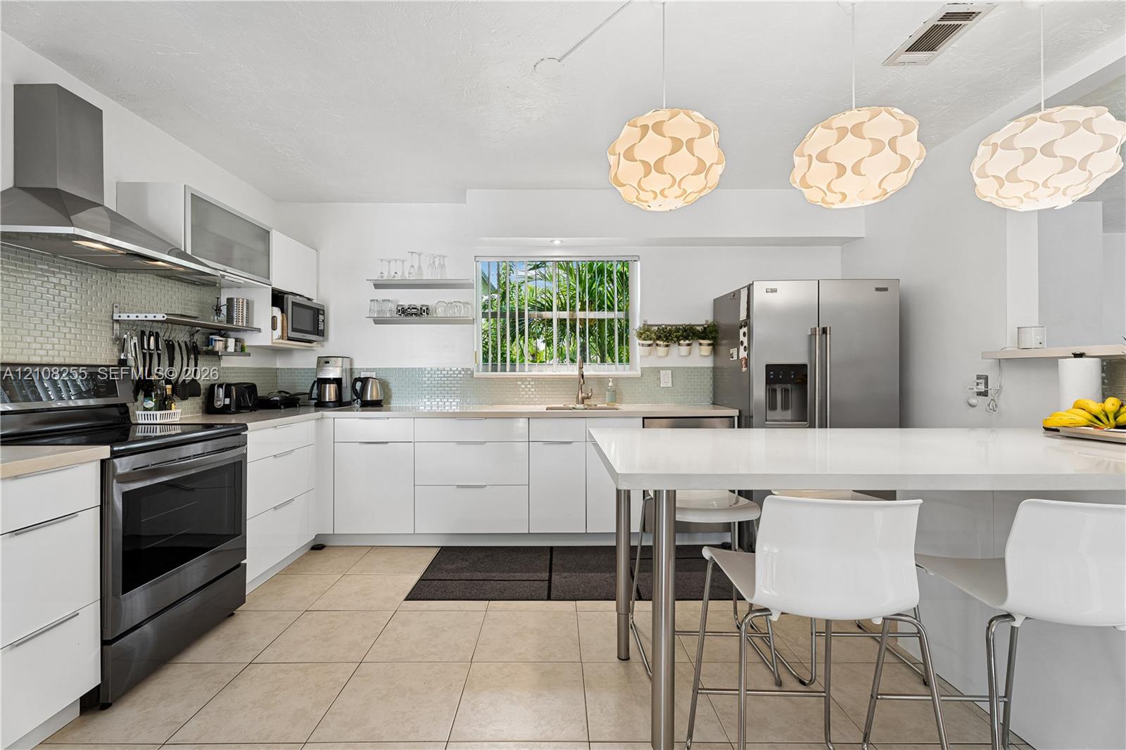 Kitchen featuring white flat-panel cabinetry, stainless steel appliances, a tile backsplash, and a central island with a solid-surface countertop