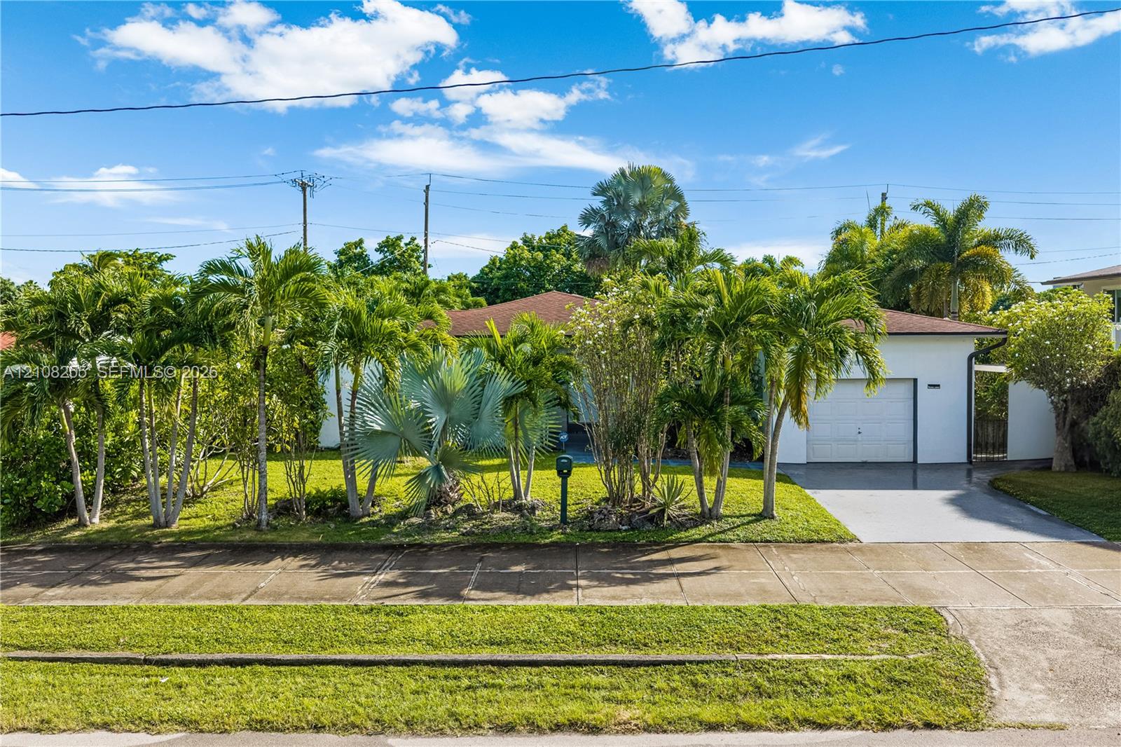 Single-story residence featuring a low-slope roof, attached one-car garage, concrete driveway, and established tropical landscaping