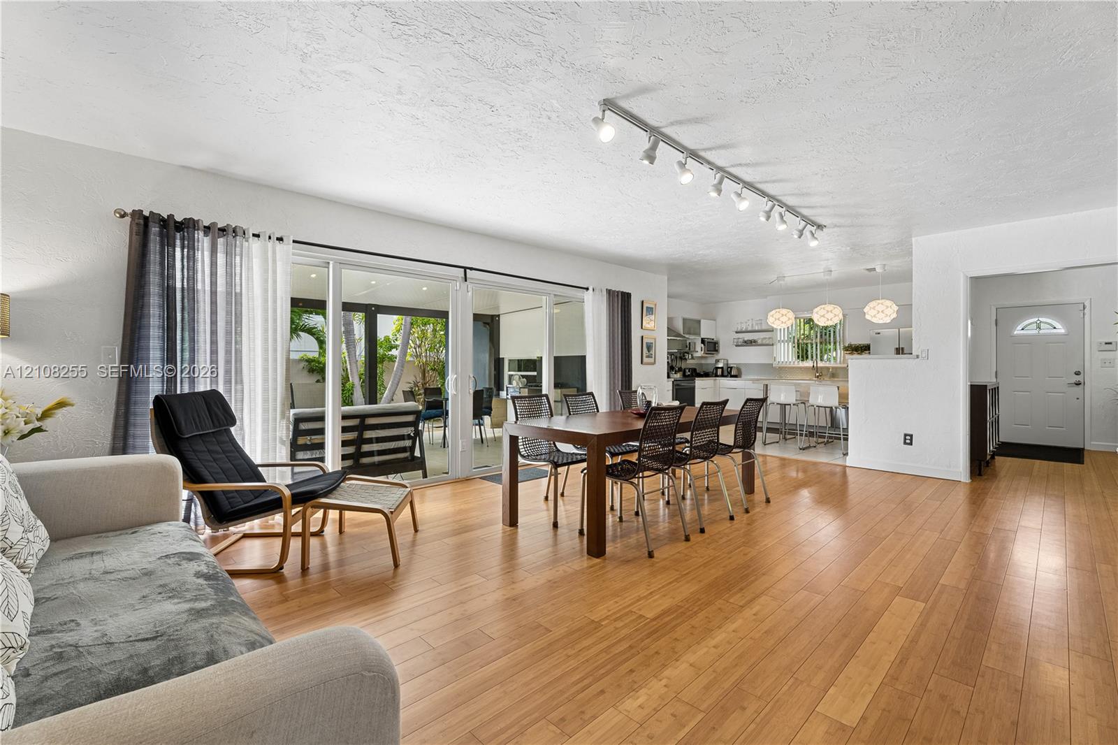 Open-concept interior with wood-finish flooring, sliding glass doors, adjustable track lighting, and a six-panel entry door