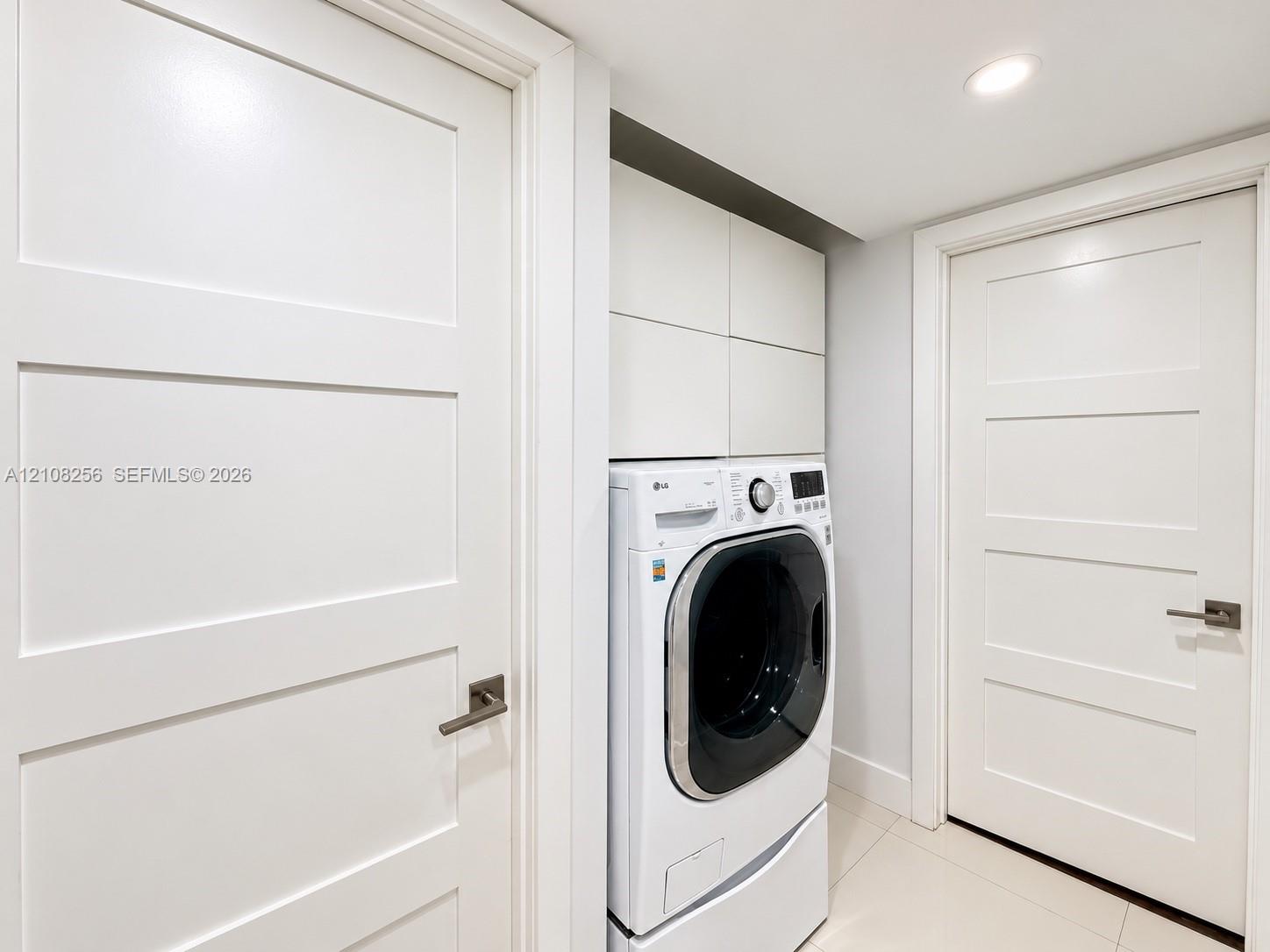 Laundry area featuring built-in cabinetry, recessed lighting, and tile flooring, framed by two white Shaker-style doors with metallic lever handles