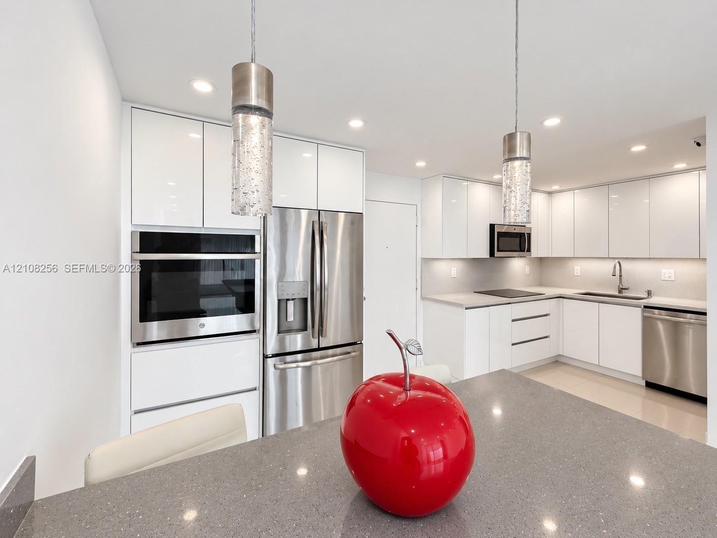 Kitchen featuring high-gloss white cabinetry, stainless steel appliances, quartz countertops, recessed lighting, and modern cylindrical pendant light fixtures
