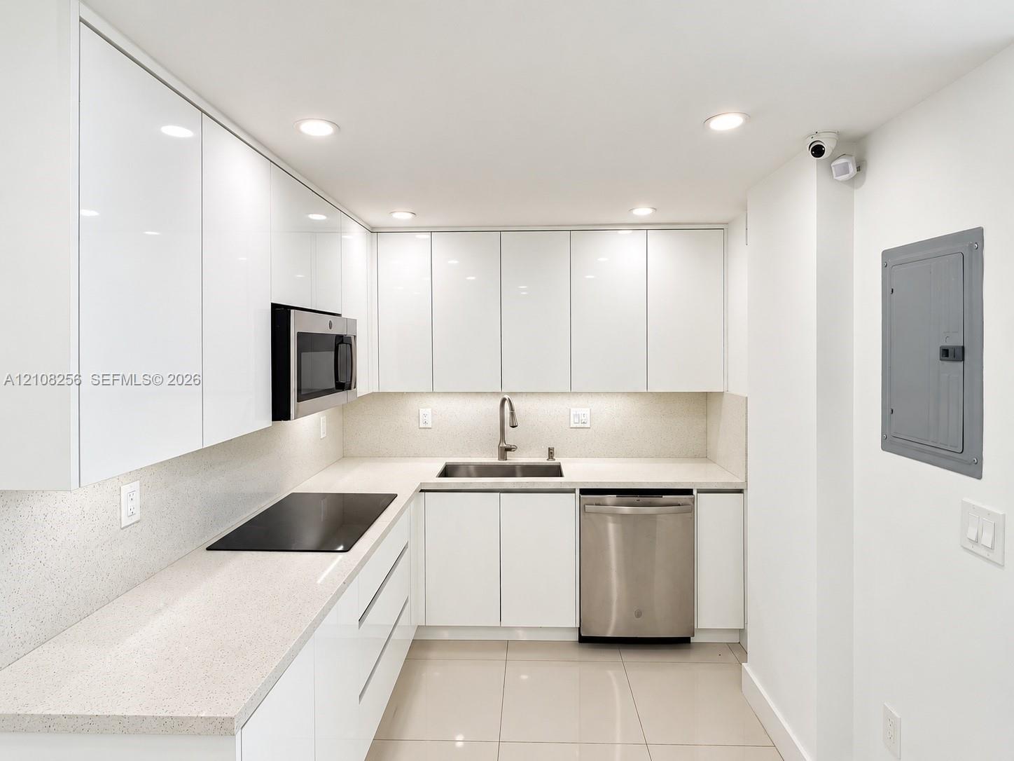 Kitchen featuring high-gloss cabinetry, light-toned stone-finish countertops, stainless steel appliances, a recessed sink with a gooseneck faucet, and porcelain tile flooring
