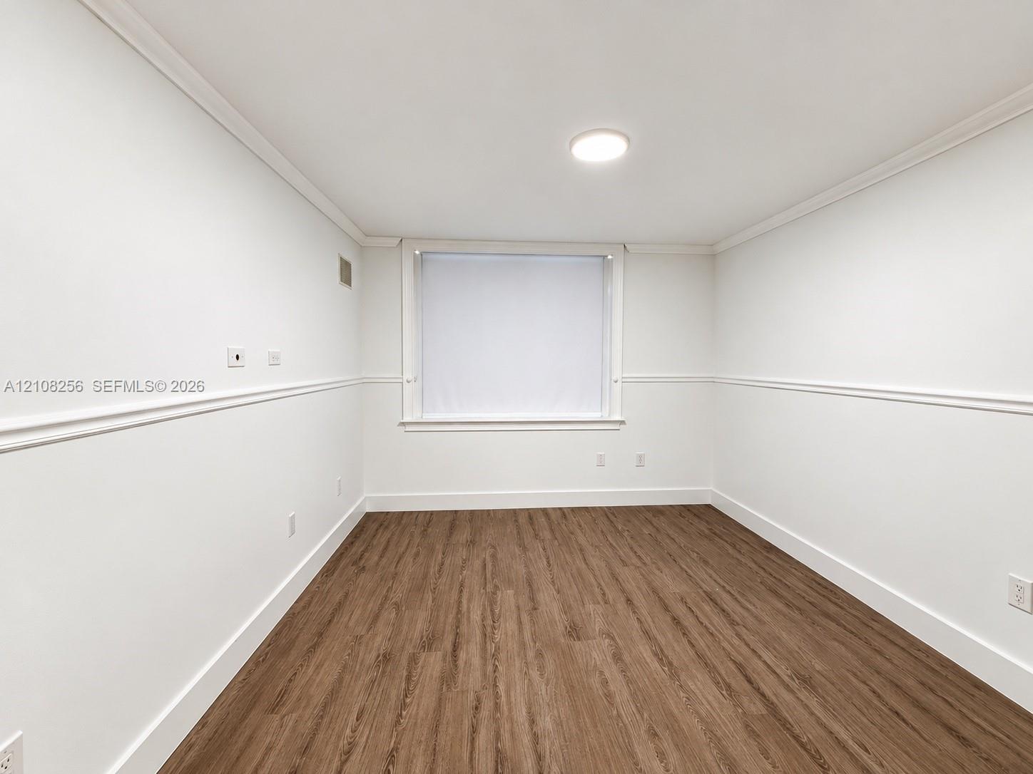 Room featuring wood-finish flooring, white walls with chair rail molding, and a flush-mount ceiling light