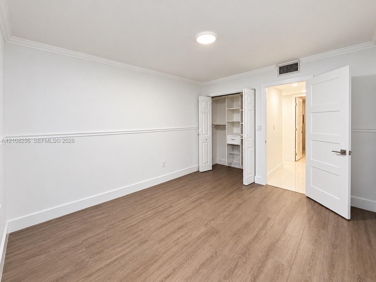 Wood-finish flooring, white walls with chair rail molding, and a closet with built-in shelving