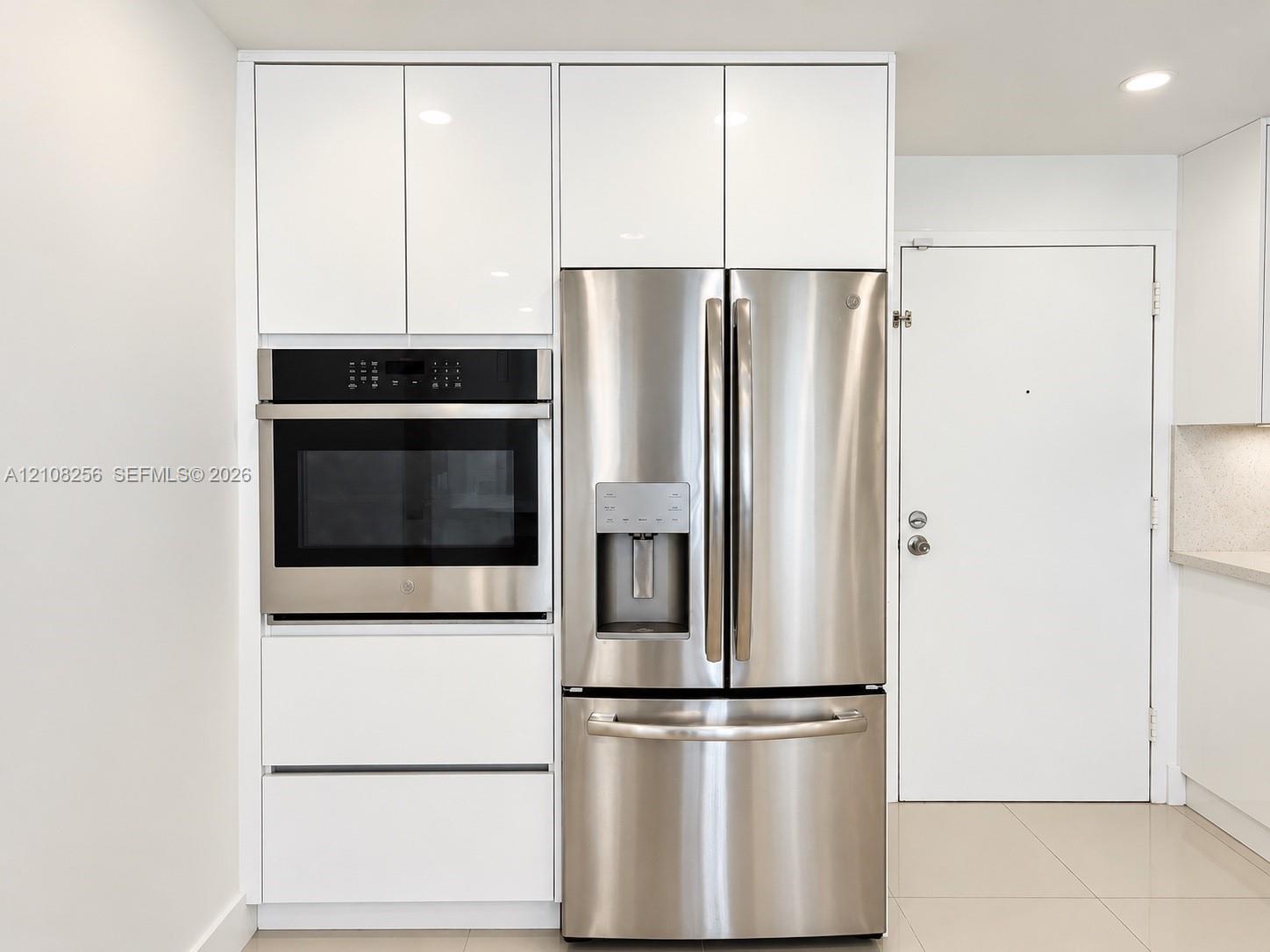 Kitchen featuring floor-to-ceiling high-gloss white cabinetry, integrated stainless steel wall oven, and French-door stainless steel refrigerator