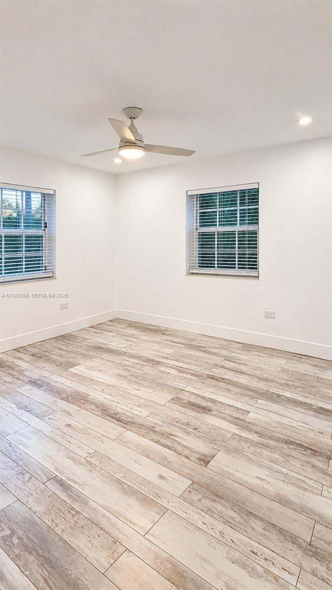 Room featuring wood-finish flooring, recessed lighting, and a ceiling fan with integrated light fixture, complemented by two windows with multi-pane glass