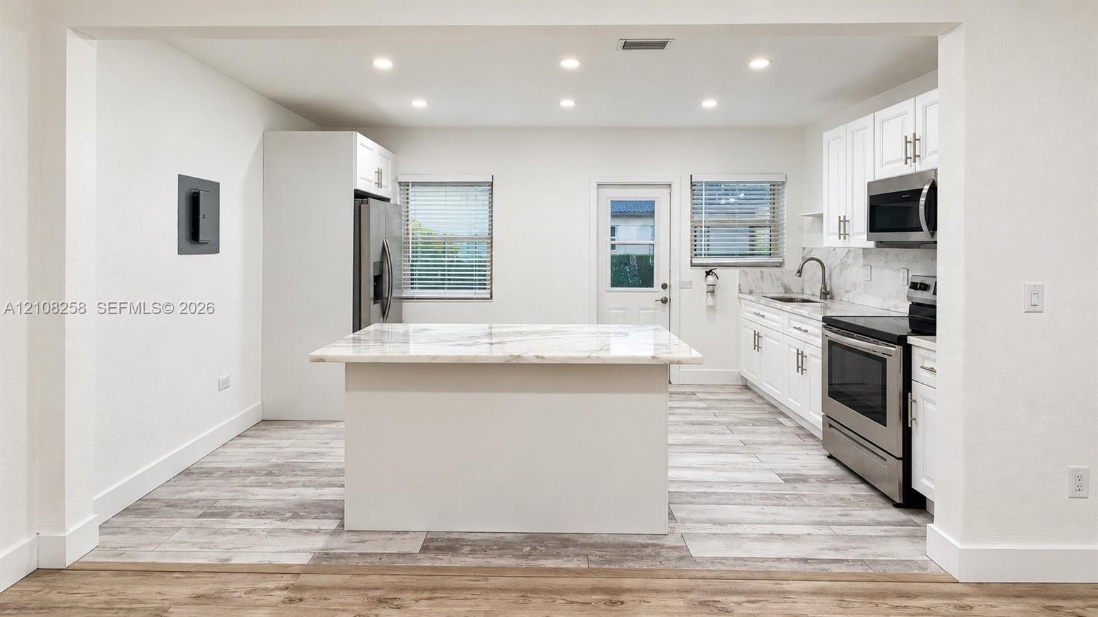 Kitchen featuring white shaker-style cabinetry, stone-finish countertops, stainless steel appliances, a center island, and wood-finish flooring