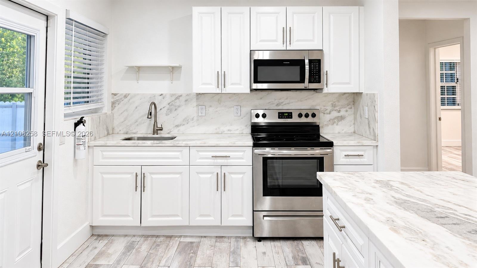 Kitchen featuring white shaker-style cabinetry, stone-finish countertops with matching backsplash, stainless steel appliances, and wood-finish flooring