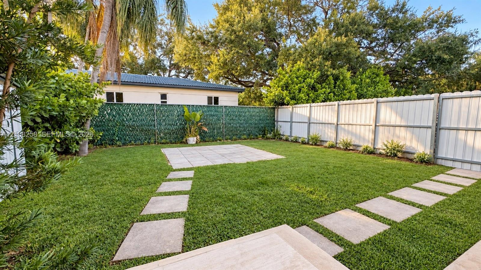 Backyard featuring a manicured lawn, stone paver walkways, a centralized stone patio, and perimeter fencing