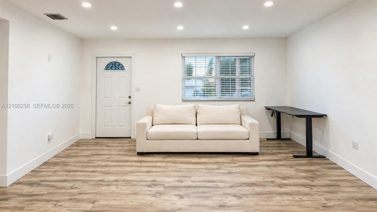 Neutral wall palette with wood-finish flooring, recessed ceiling lighting, and a single-entry door with an arched decorative glass insert