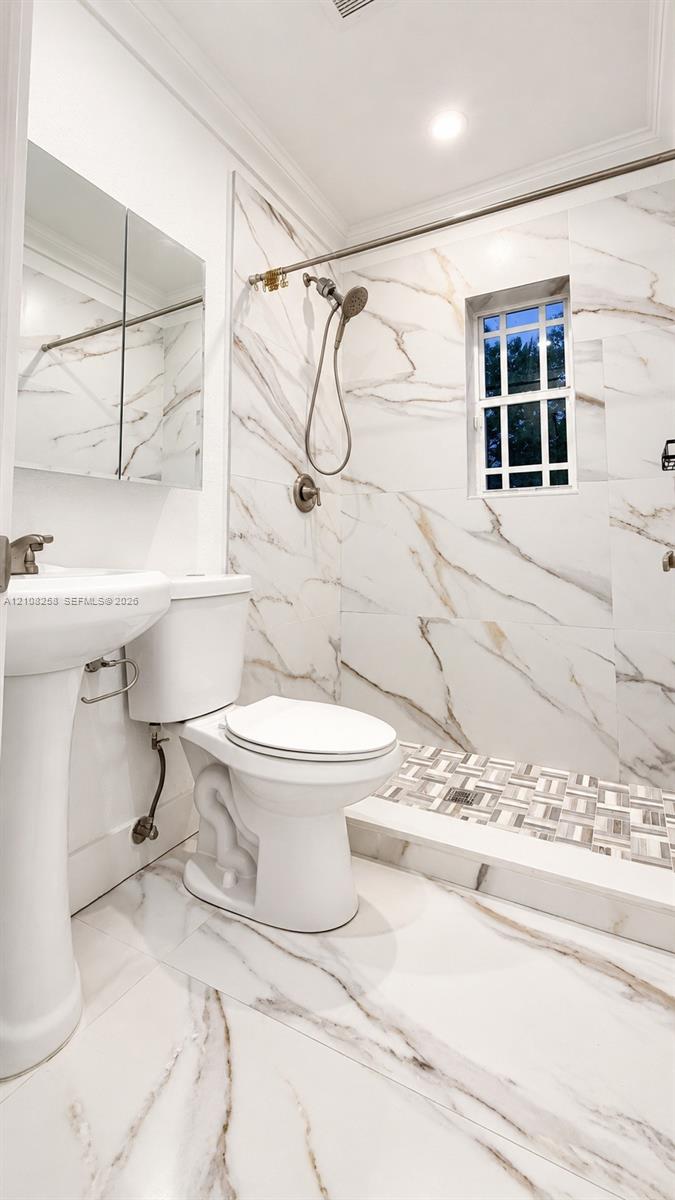 Bathroom featuring floor-to-ceiling large-format stone-patterned tile, walk-in shower with decorative mosaic tile flooring, pedestal sink, and built-in medicine cabinet