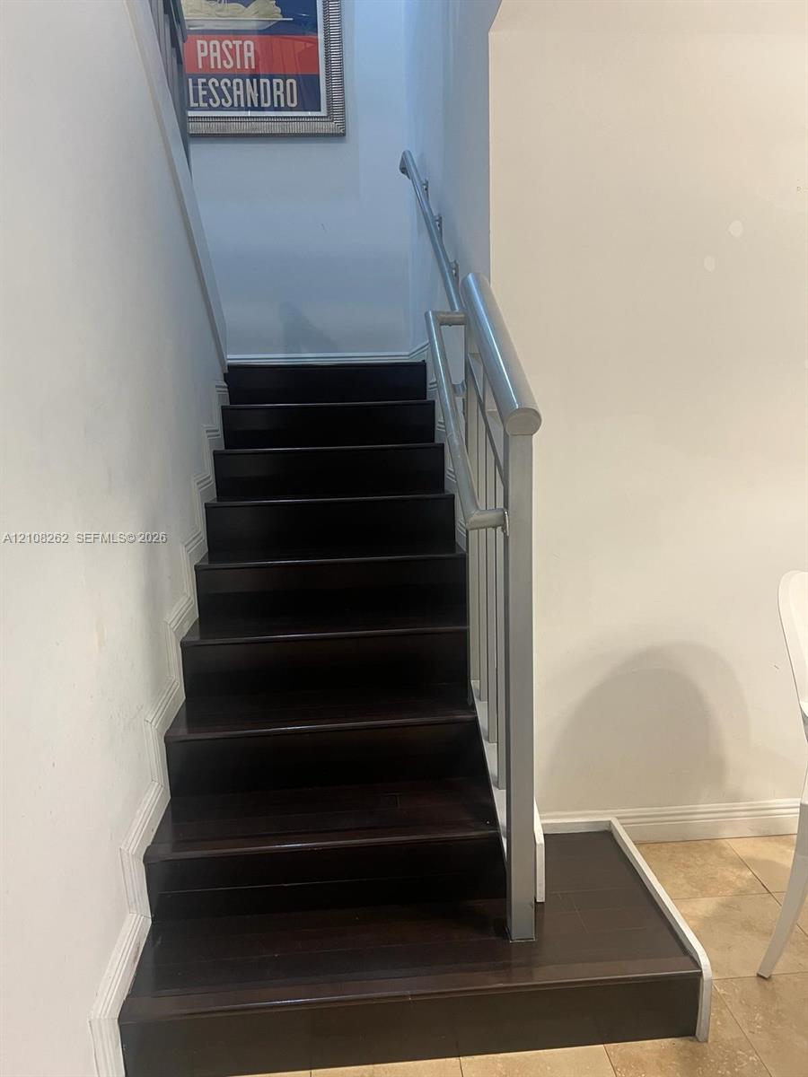 Staircase featuring dark wood-finish treads and a metallic handrail with vertical balusters