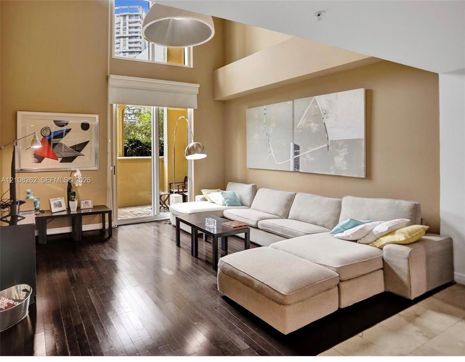 Double-height ceilings featuring an expansive clerestory window, wood-finish flooring, and sliding glass doors leading to a private balcony Double-height ceilings featuring an expansive clerestory window, wood-finish flooring, and sliding glass doors leading to a private balcony