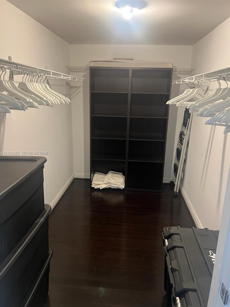 Walk-in closet featuring dark wood-finish flooring, dual-tier wire shelving, and floor-to-ceiling built-in shelving