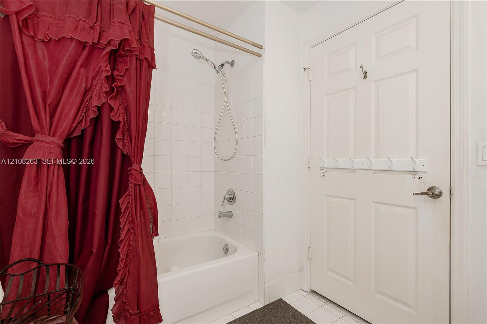 Bathroom featuring a white composite bathtub, wall-mounted shower head, tiled surround, and a six-panel door with integrated hardware