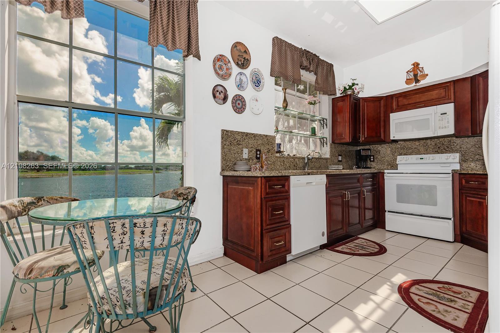 Kitchen featuring raised-panel wood cabinetry, stone countertops, tiled flooring, and floor-to-ceiling windows with water scenery