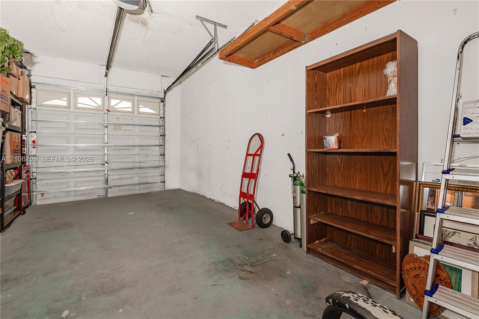 Garage space featuring an overhead sectional garage door with inset windows, concrete flooring, and mounted overhead storage shelving