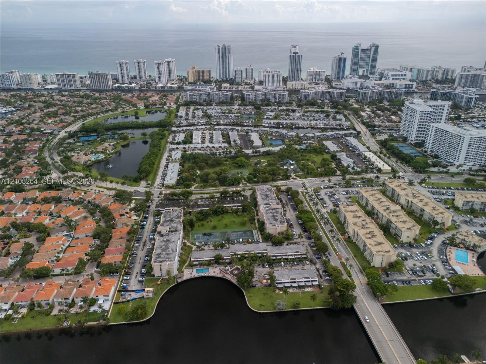 Aerial perspective of a multi-building residential complex featuring waterfront exposure, multiple swimming pools, tennis courts, and landscaped green space