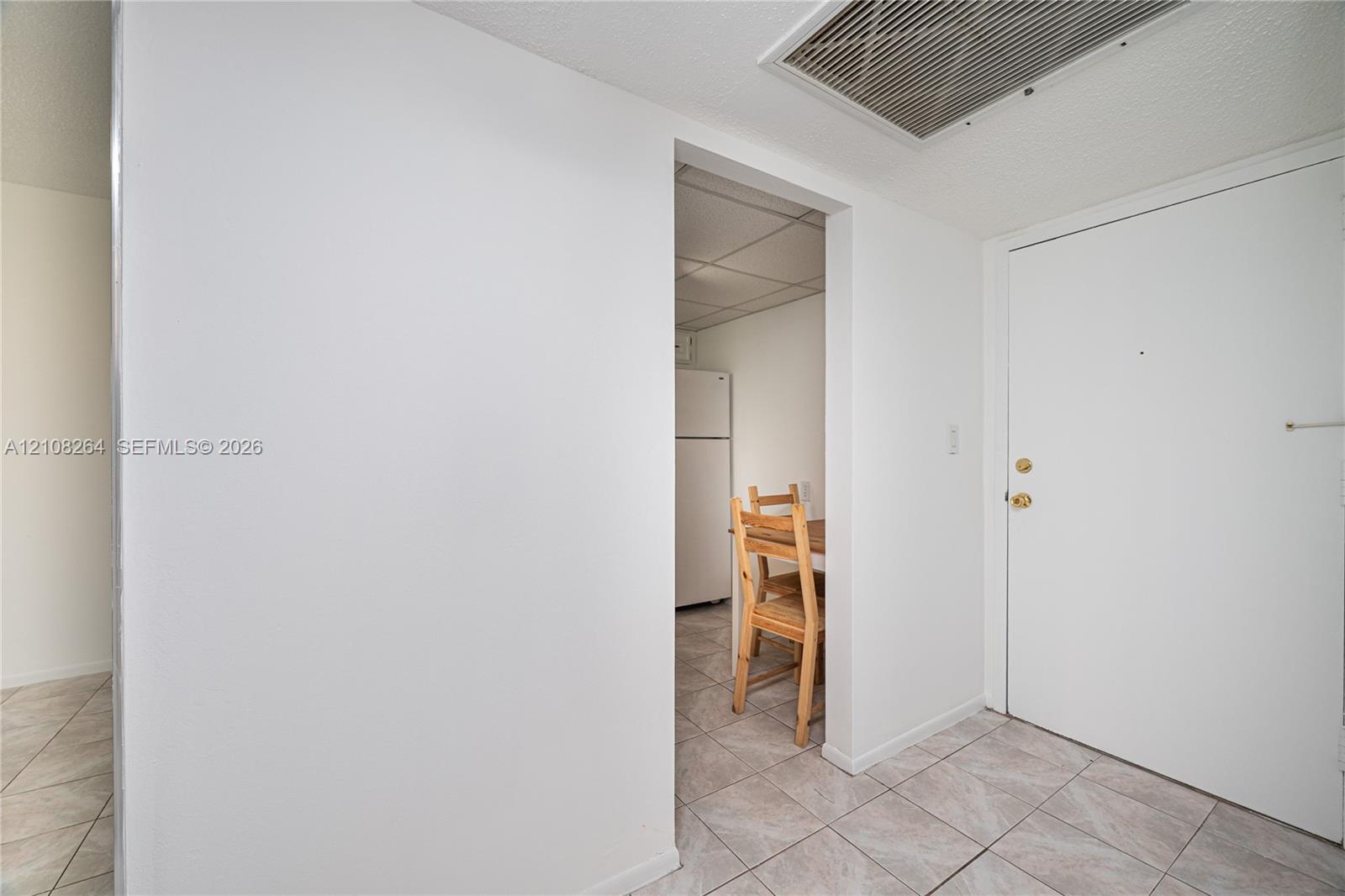Entryway featuring light-toned tile flooring, a solid panel entry door with metallic hardware, and a high-clearance doorway