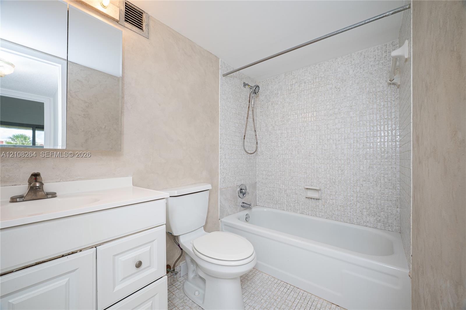 Bathroom featuring a white vanity cabinet with a solid surface countertop, mirrored medicine cabinet, wall-mounted shower head, and mosaic tile surround in the tub area