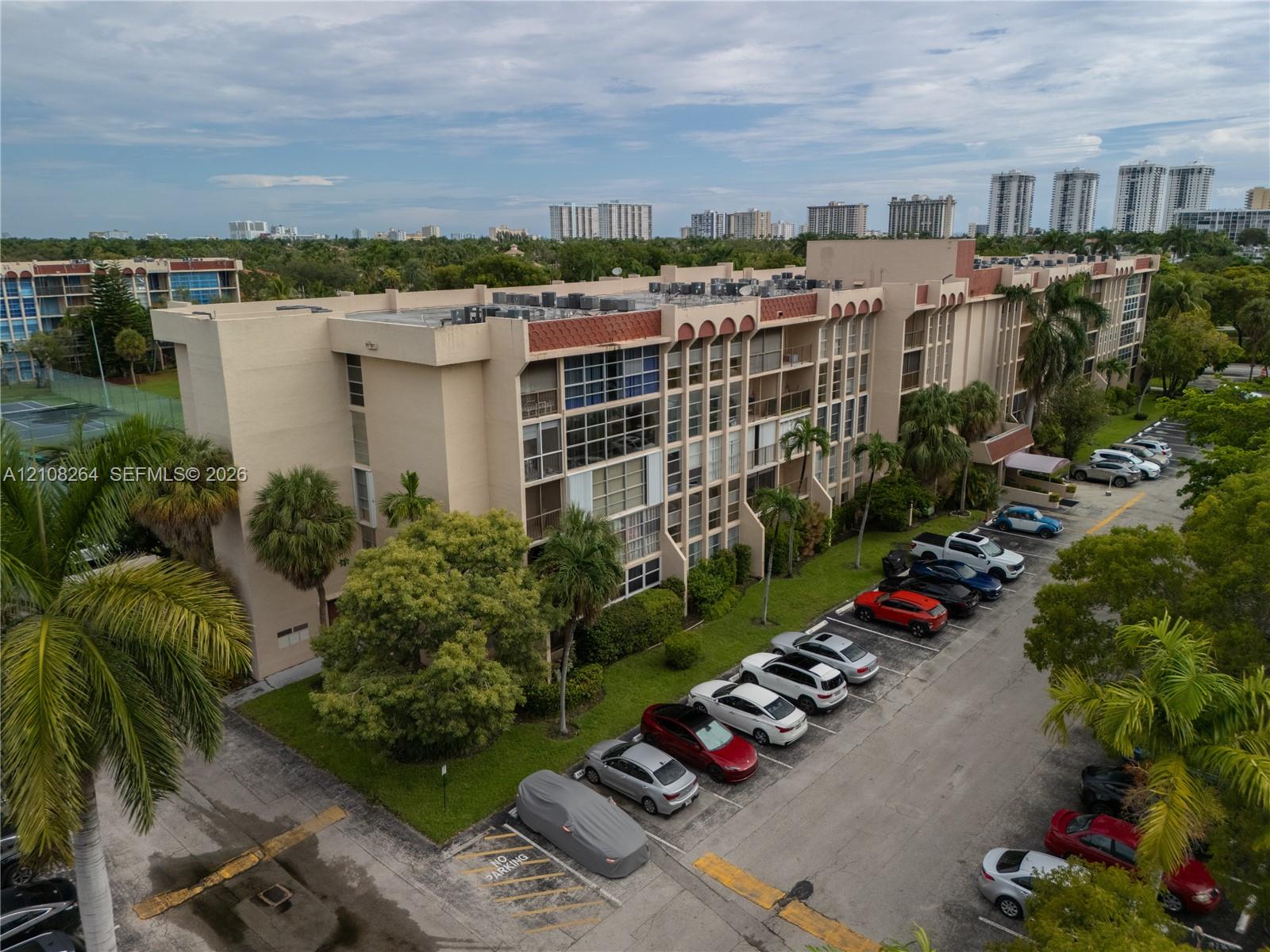 Multi-story architectural exterior featuring recessed balconies, concrete facade, flat roofline, and mature landscaping