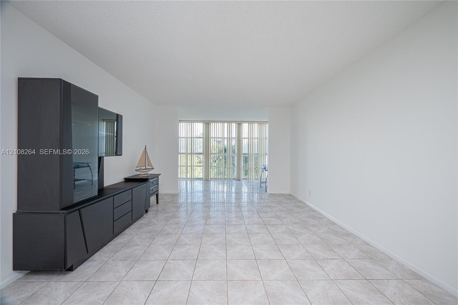 Open-concept living space featuring neutral ceramic tile flooring, floor-to-ceiling windows, and vertical blinds Open-concept living space featuring neutral ceramic tile flooring, floor-to-ceiling windows, and vertical blinds