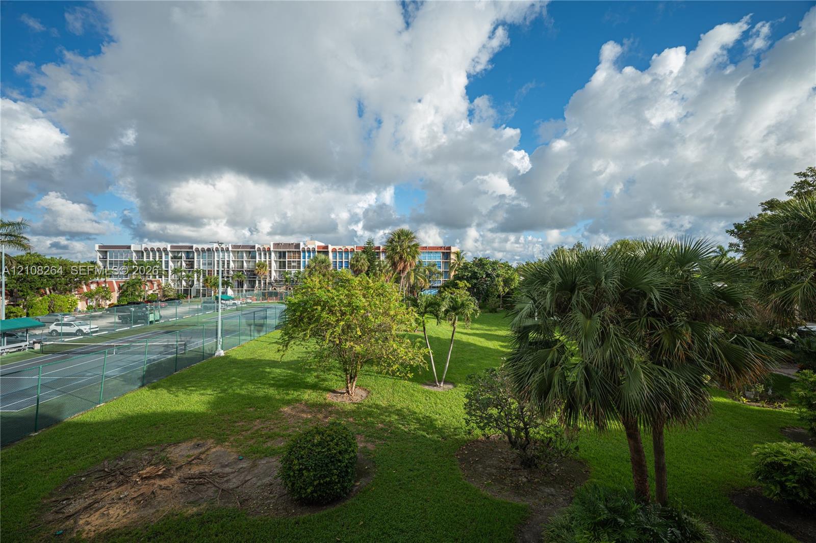 Fenced tennis court, expansive green space, mature palm trees, and lush landscaping
