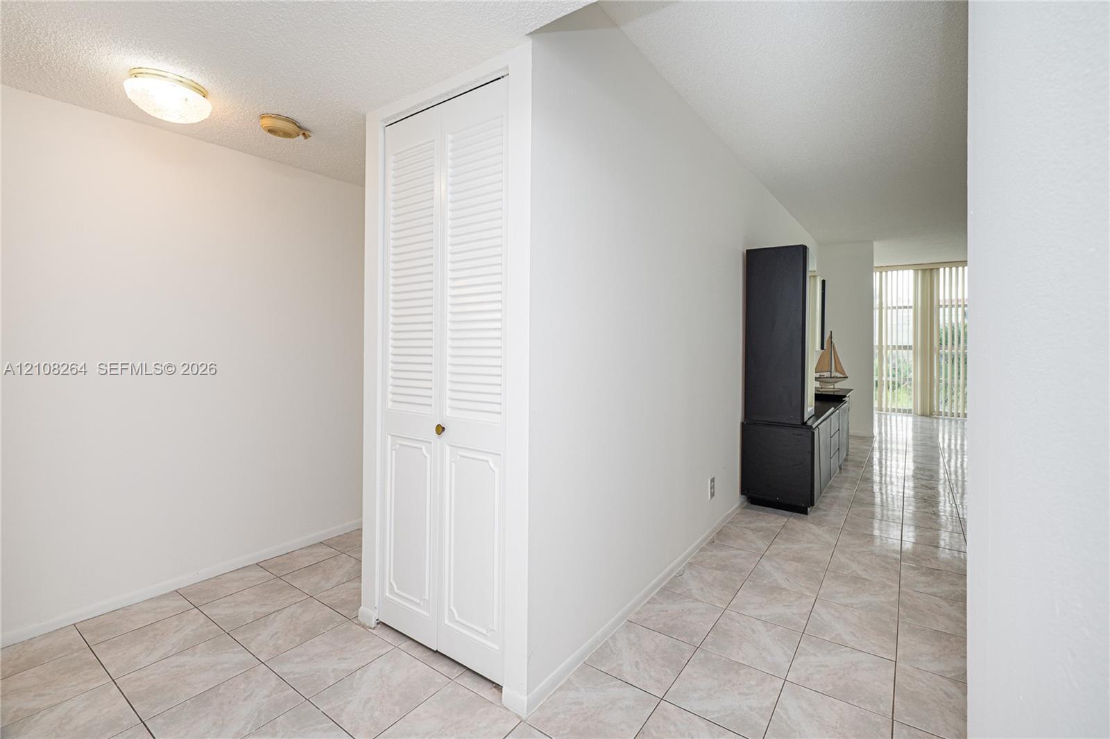 Neutral ceramic tile flooring, white louvered-panel closet doors, and floor-to-ceiling vertical blinds