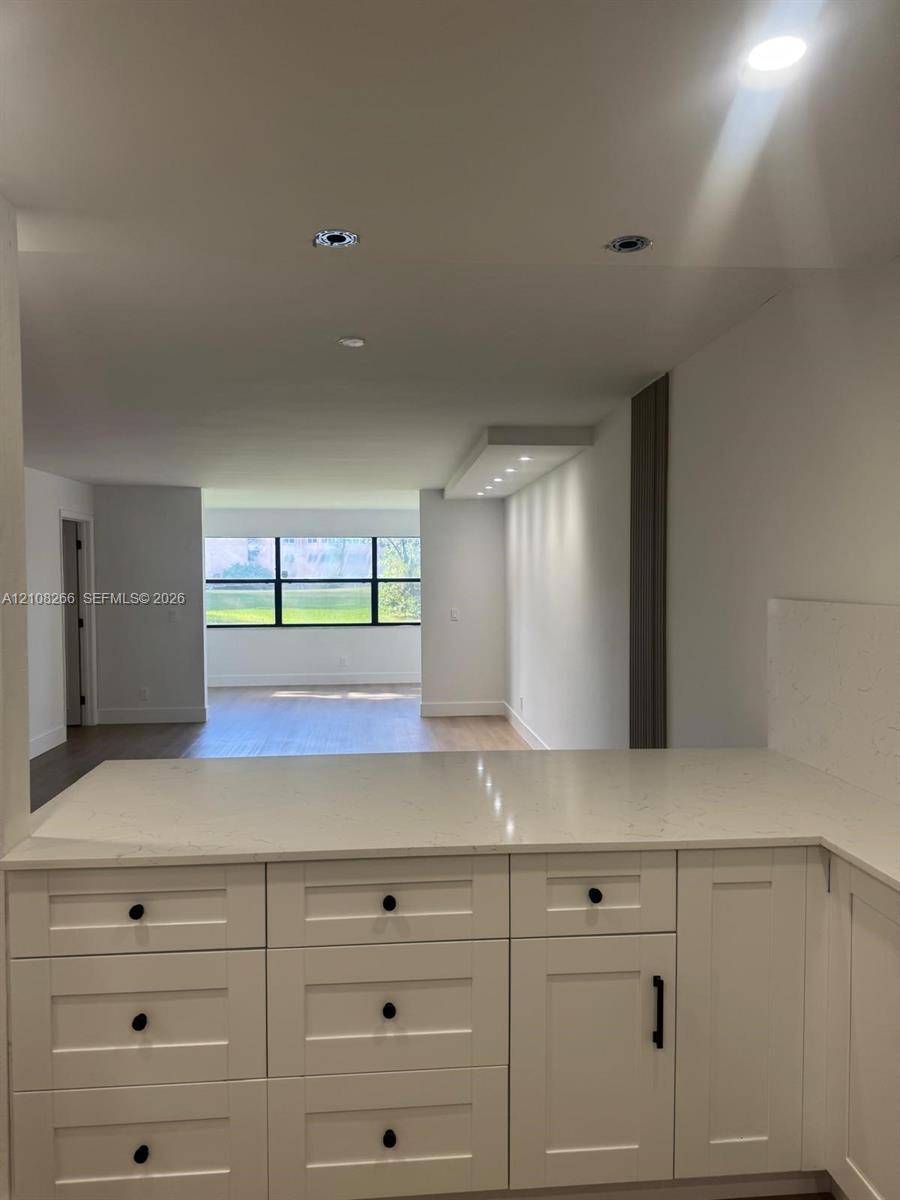 White Shaker-style cabinetry featuring matte black hardware, stone-finish countertops, recessed ceiling lighting, and wood-finish flooring