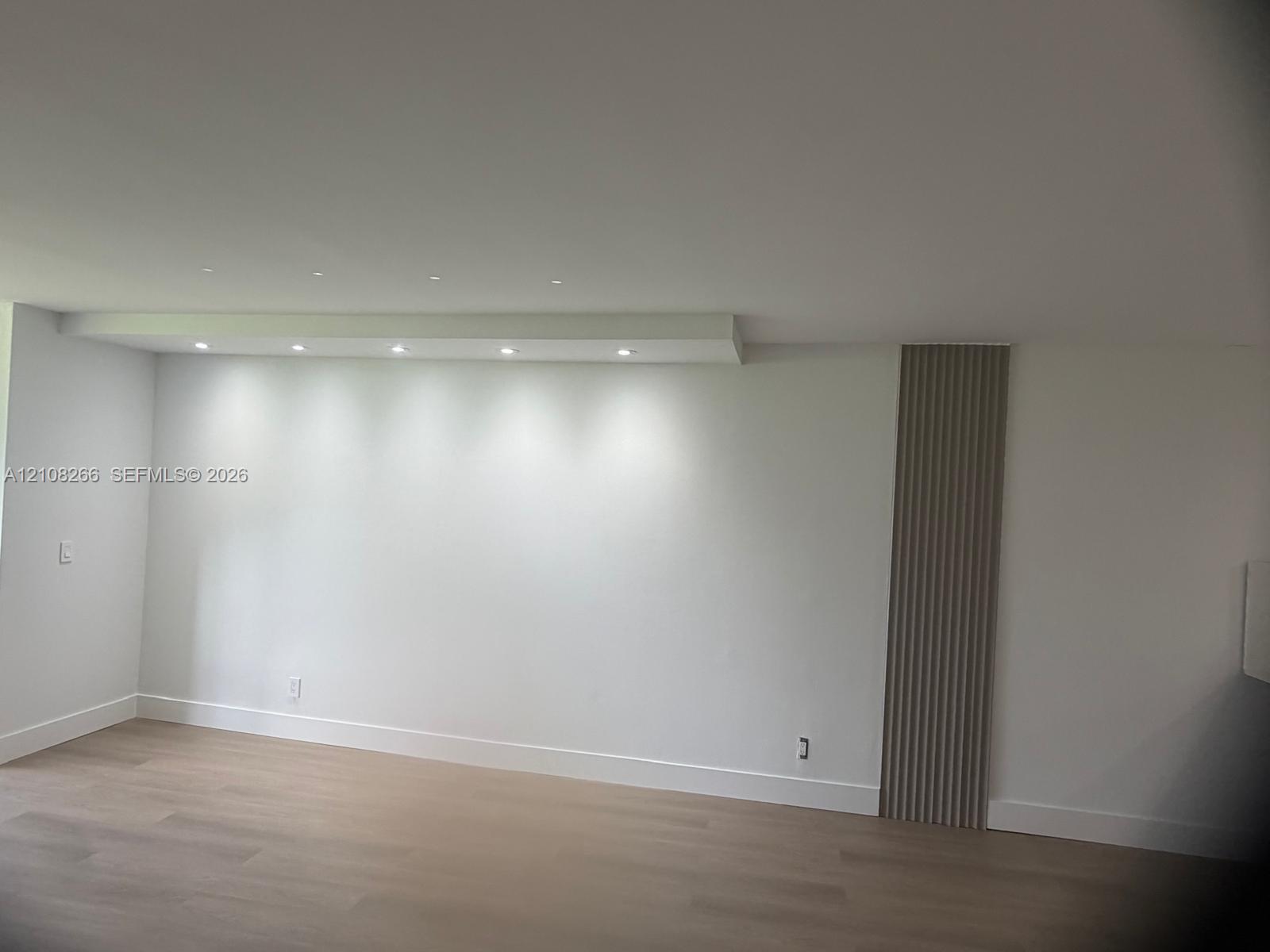 Minimalist interior featuring recessed ceiling lighting, light-toned wood-finish flooring, and a decorative vertical slat accent wall