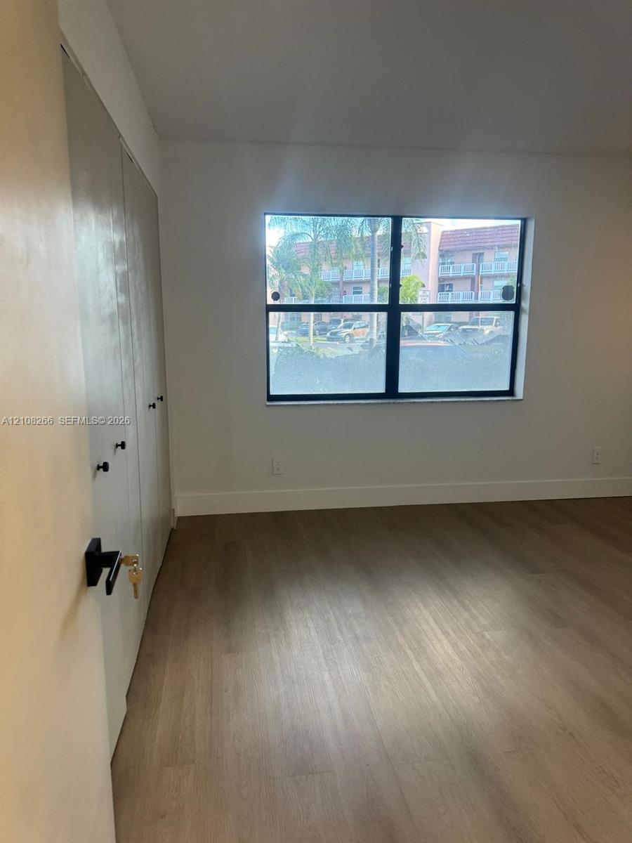 Interior space featuring wood-finish flooring, a multi-panel window with a dark frame, and built-in closet storage with matte black hardware