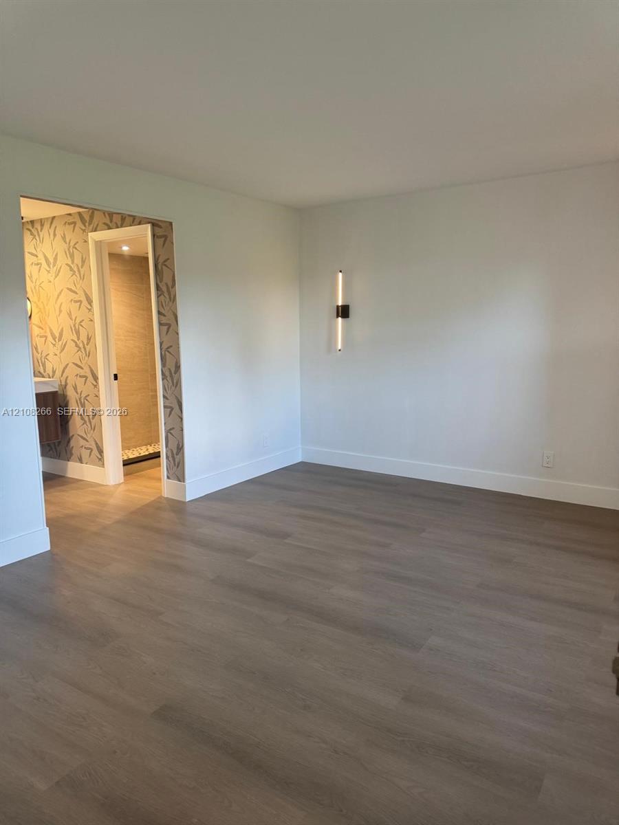 Wood-finish flooring, minimalist wall-mounted linear lighting, and patterned wall covering surrounding an interior doorway