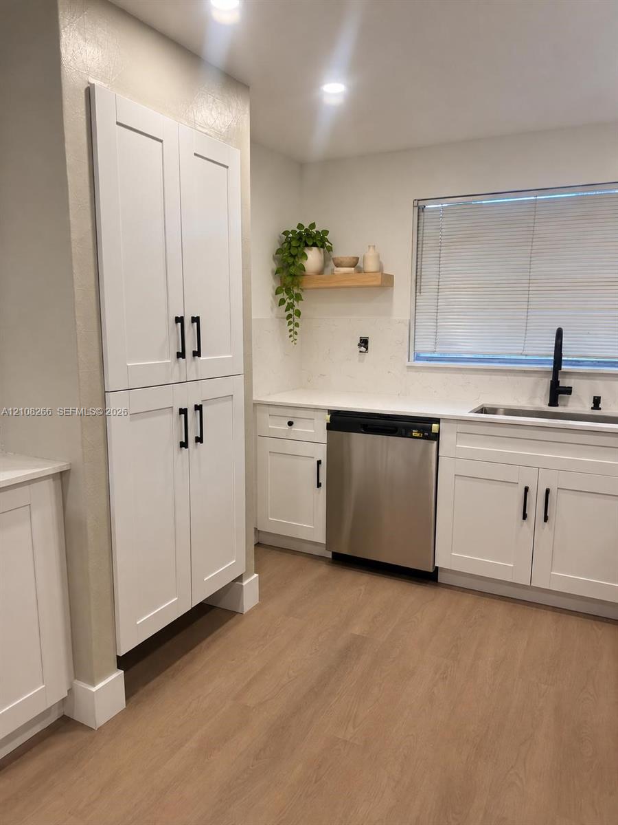 White Shaker-style cabinetry featuring matte black hardware, stone-finish countertops, stainless steel dishwasher, undermount sink with a matte black faucet, and wood-finish flooring