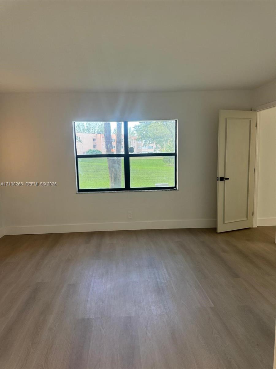 Interior room featuring light-toned wood-finish flooring, a single-pane window with black framing, and a white recessed-panel door with matte black hardware