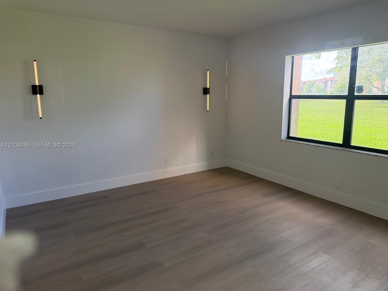 Neutral-toned wood-finish flooring, two modern vertical wall-mounted fixtures, and a large window with black framing