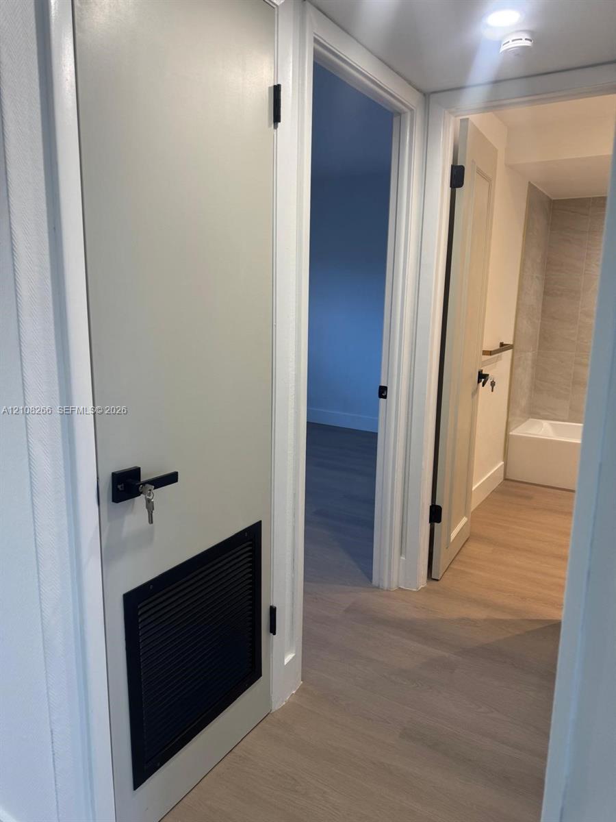 Interior hallway featuring wood-finish flooring, white doors with matte black hardware, and an integrated black door ventilation grille