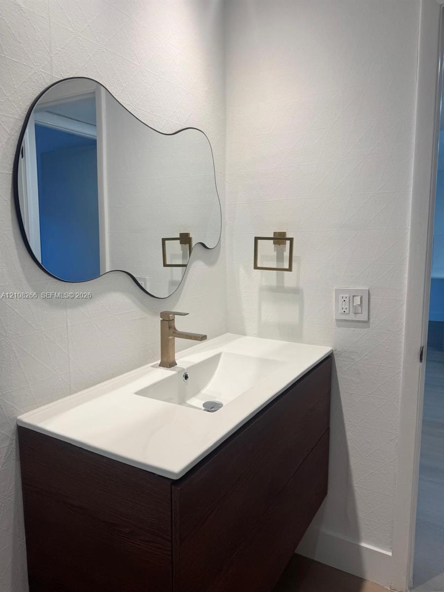 Floating vanity with dark wood-finish cabinetry, white countertop, integrated sink, metallic finish faucet, and organic-shaped mirror