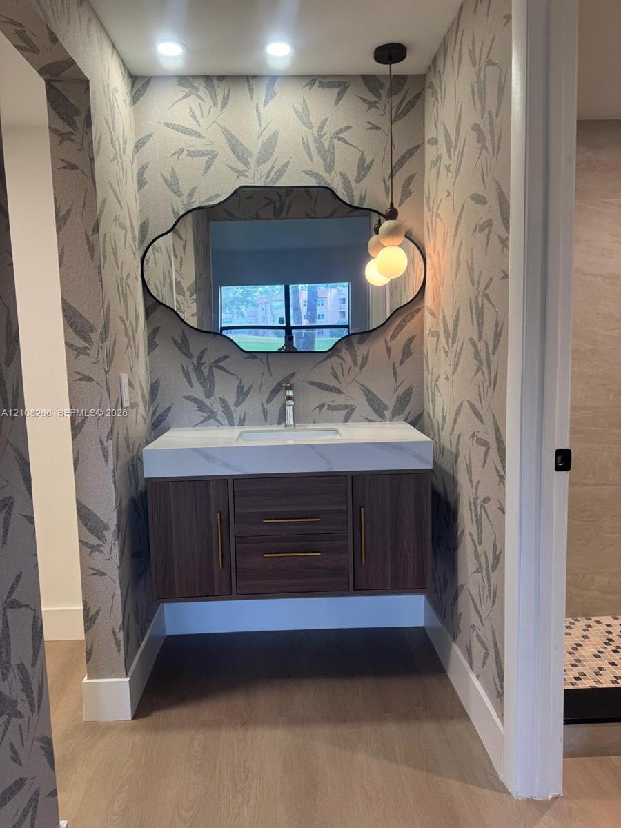 Floating wood-finish vanity with a rectangular sink, quartz countertop, custom-shaped wall mirror, and modern pendant lighting