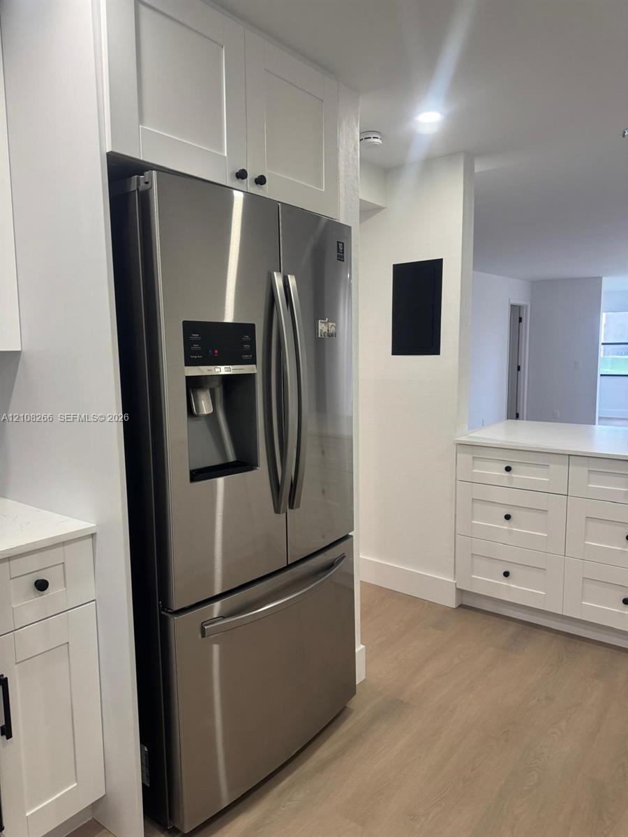 Kitchen featuring white shaker-style cabinetry, wood-finish flooring, stainless steel French door refrigerator, and white countertops