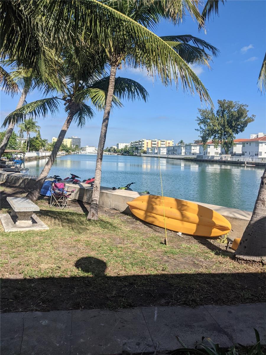 Waterfront grounds featuring a concrete bulkhead, mature palm trees, and a stone bench