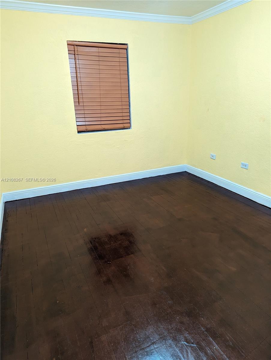 Interior room featuring dark-stained wood-finish flooring, light-colored walls, crown molding, and a recessed window with horizontal blinds