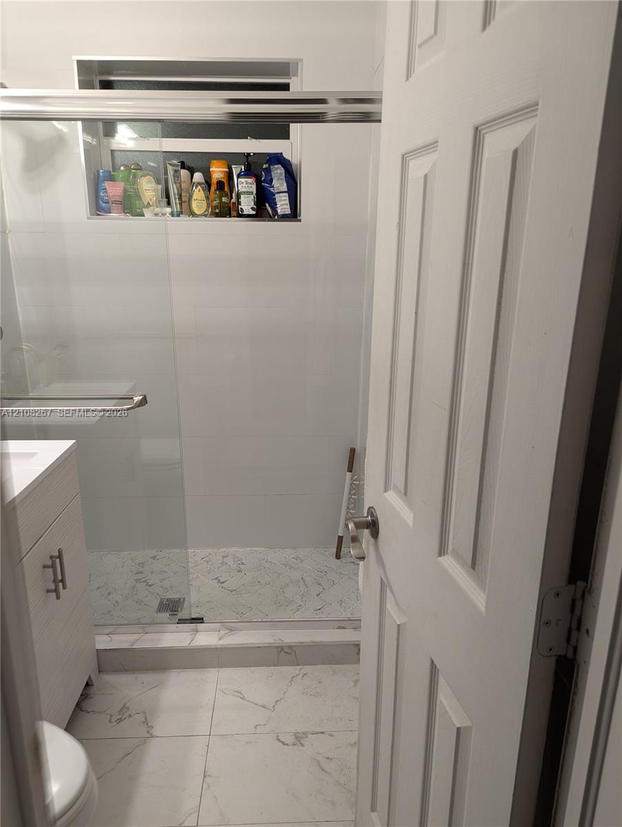 Bathroom featuring a walk-in shower with a glass enclosure, built-in tiled niche, stone-patterned floor tiling, and a vanity with a white cabinet