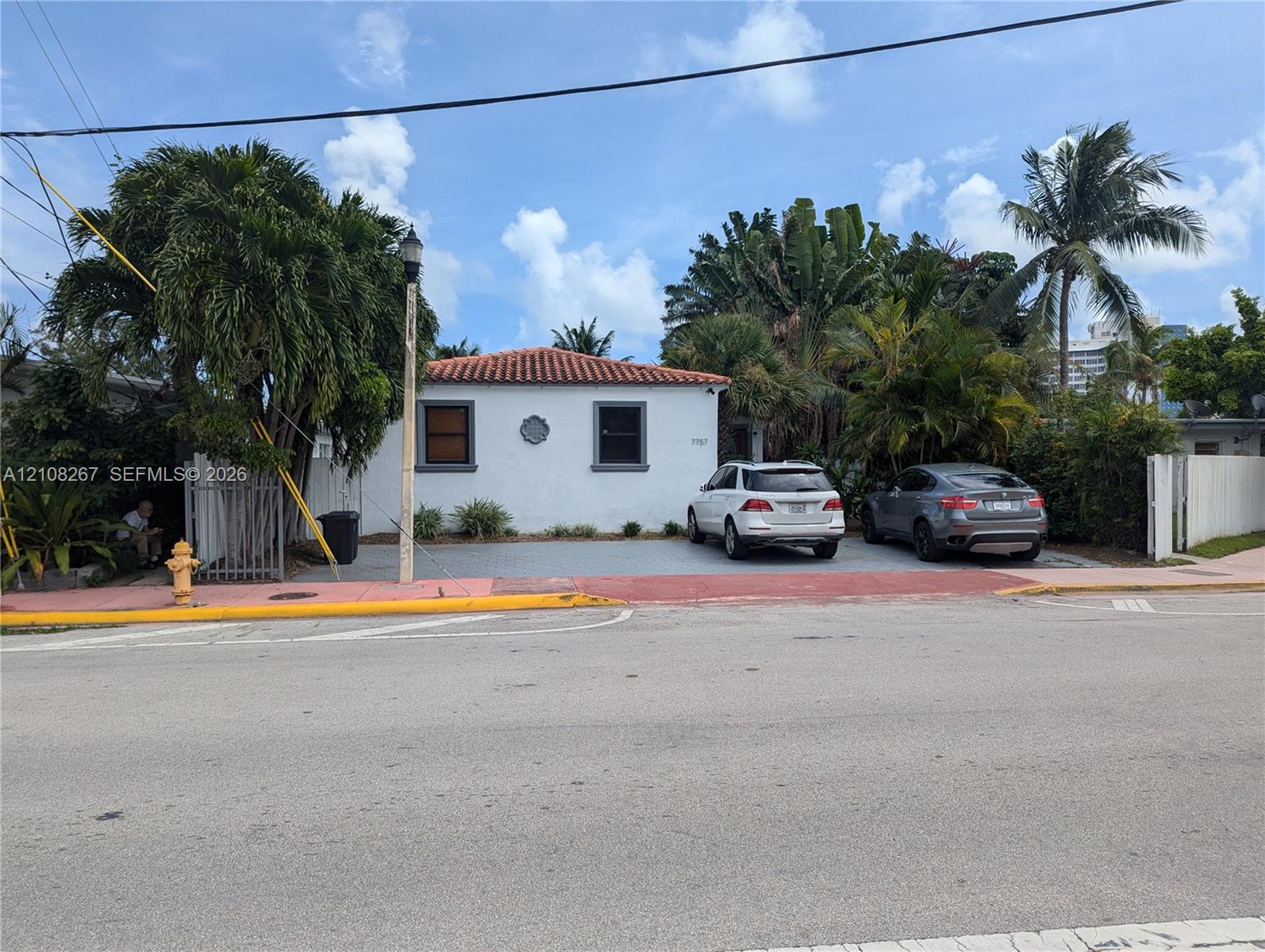 Stucco exterior featuring a terracotta-tiled hip roof, multi-car paved parking area, and mature tropical landscaping