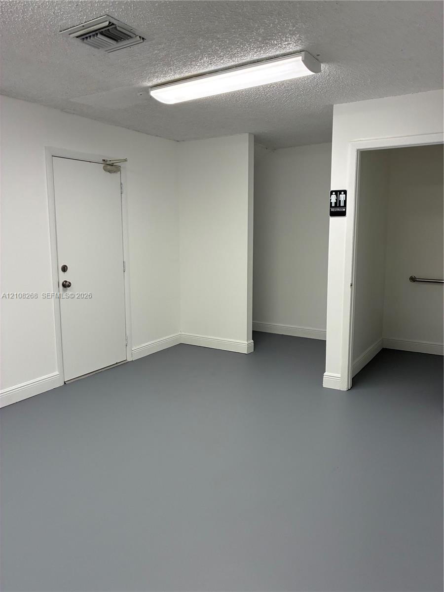 Neutral-toned interior space featuring solid-surface flooring, flush-mount lighting, and a metal-clad entry door