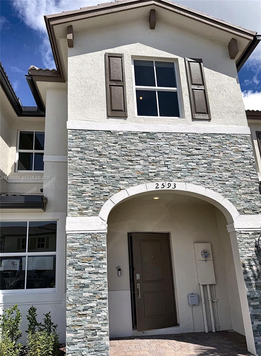 Exterior facade featuring a combination of stucco and stone veneer, arched entryway, dark-finish shutters, and multi-pane windows