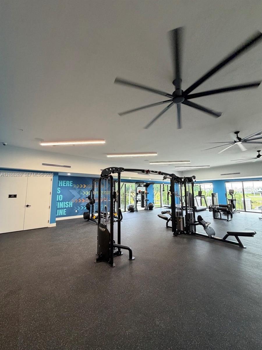 Fitness center featuring high-contrast rubberized flooring, large-diameter ceiling fans, linear recessed lighting, and floor-to-ceiling windows