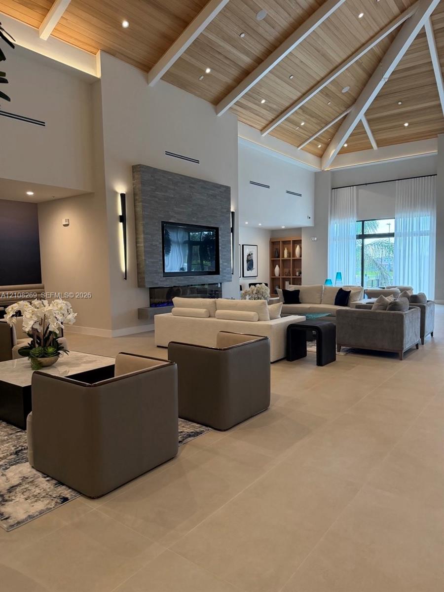 Vaulted ceiling with wood-finish paneling and exposed beams, stacked stone fireplace surround, recessed lighting, and large-format tile flooring